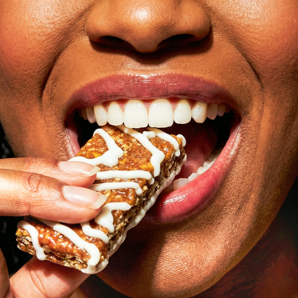 Close-up of a person biting into a granola bar with white drizzle.